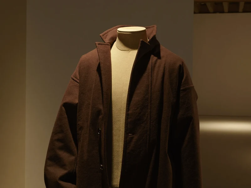 Schneiderbüste mit dunklem Wollmantel im gedämpft beleuchteten, museumsartigen Atelier