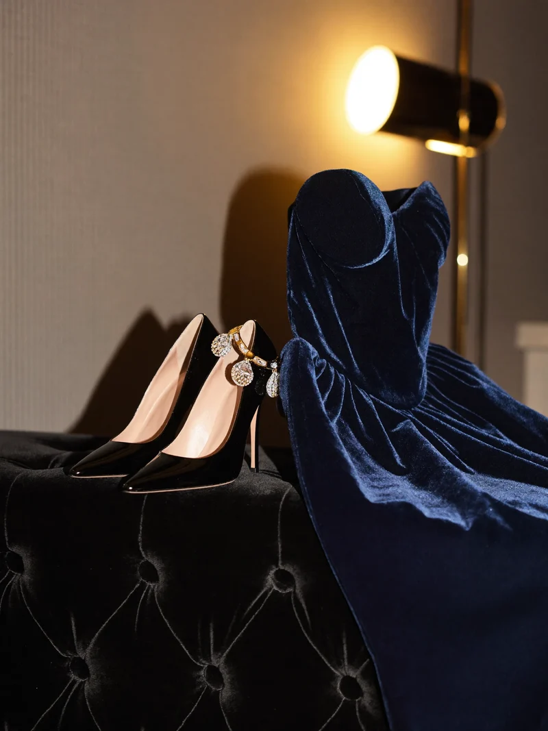 Abendkleid, Schuhe und Ohrringe arrangiert auf einer Samtbank unter warmer Lampe