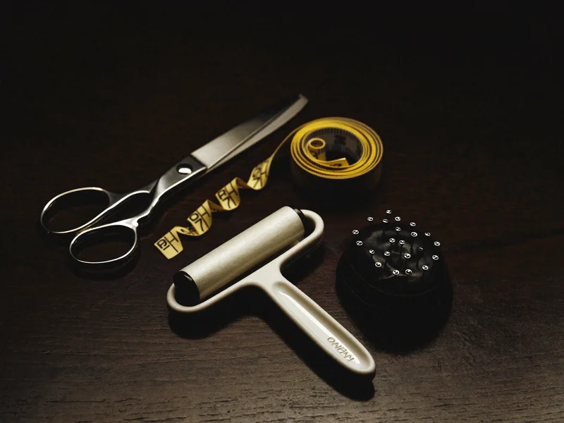 Schere, Nadeln, Massband und Fusselroller als Styling-Set auf dunklem Holz
